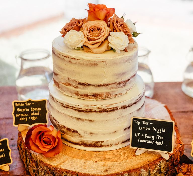 Two tier semi-naked rustic wedding cake with toffee, orange and white rose flower decorations