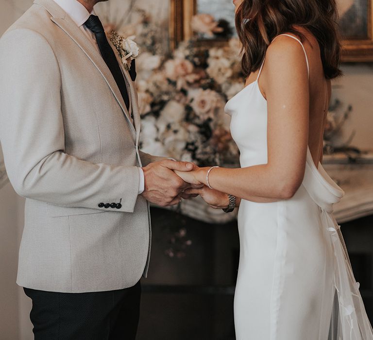 Groom wearing a grey suit jacket holding hands with the bride in a white satin backless wedding dress 