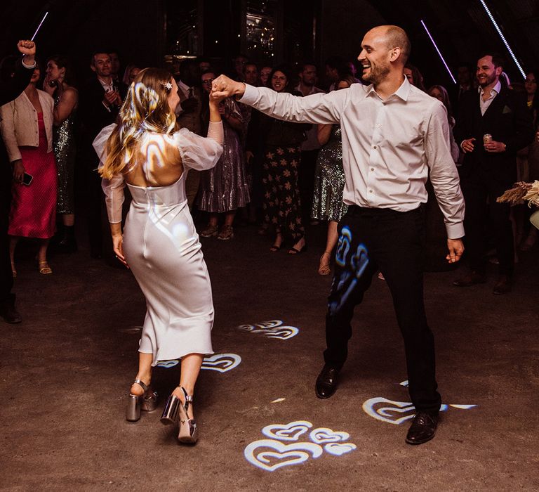 Bride and groom have their first dance together under cool wedding lighting of different chandeliers 