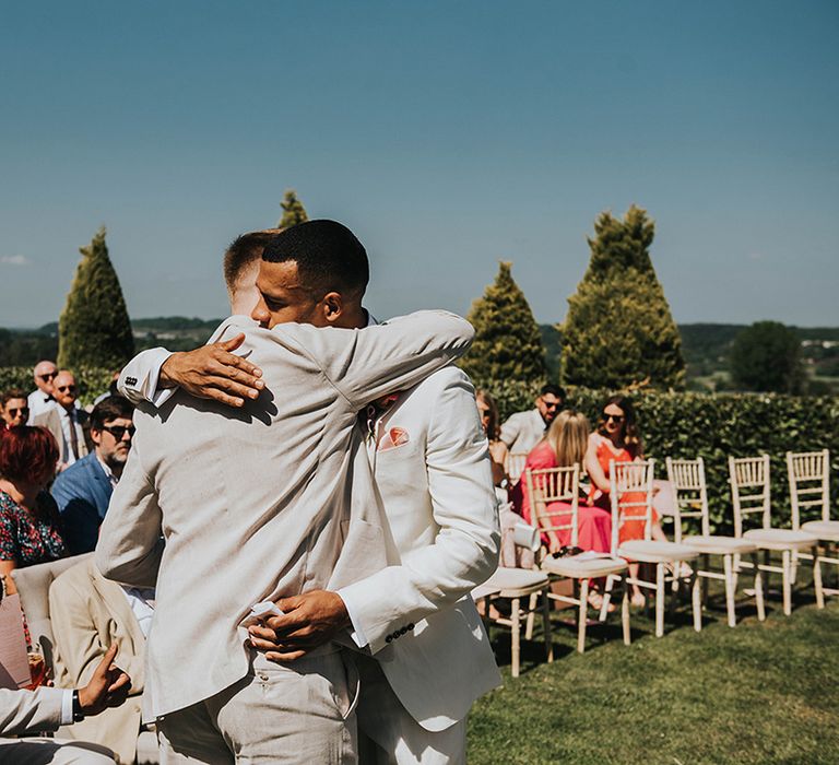 Groom hugging his groomsmen before the wedding ceremony in matching cream suits