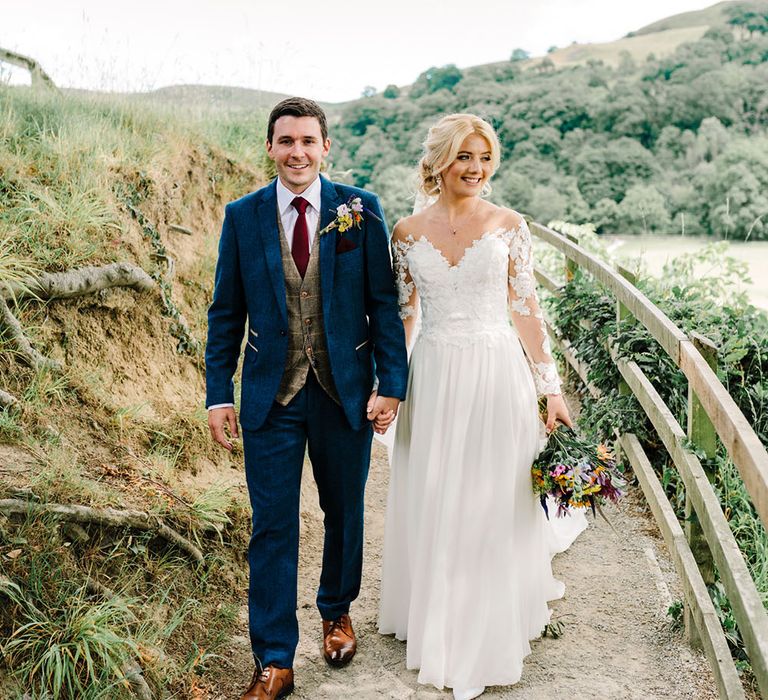 Bride & groom walk through the countryside as bride holds bright floral bouquet 