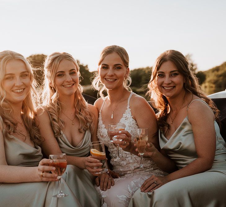 Bride sits with her bridesmaids in silk satin bridesmaid dresses in boat as the sun begins to set 