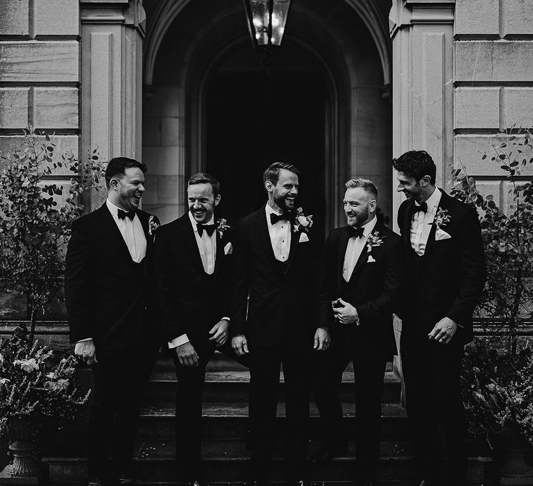 Black and white shot of the groom and the groomsmen standing outside the entrance to Callow Hall wedding venue