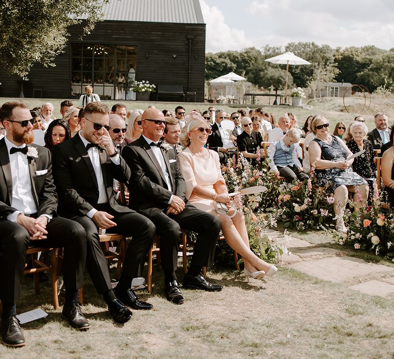 Wedding guests in black-tie watch ceremony outdoors at Botley Hill Barn 