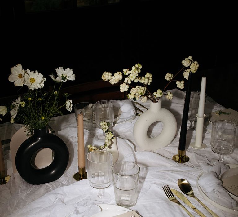 Minimalistic wedding tablescape with white tablecloth, gold cutlery, black and white table decorations and monochrome tapered candles 