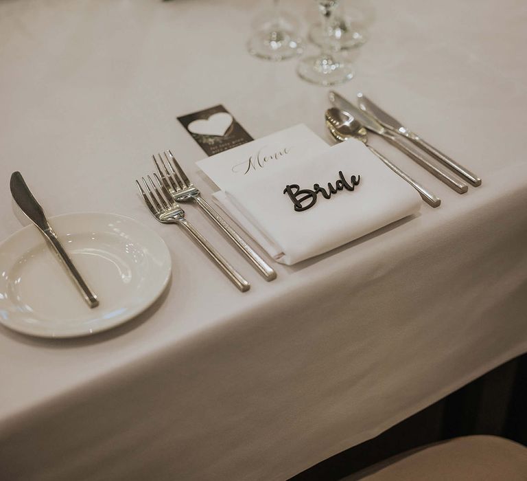 Classic and clean all white wedding tablescape with personalised laser cut place names with silver cutlery and white flowers