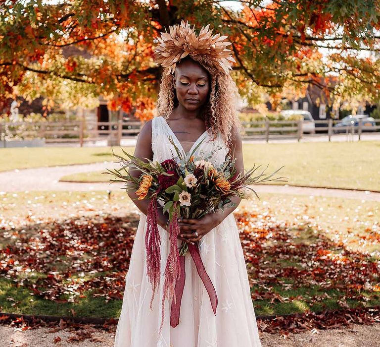 Bride in star embroidered peach floaty wedding gown holding autumnal dried flowers and large golden bridal crown 