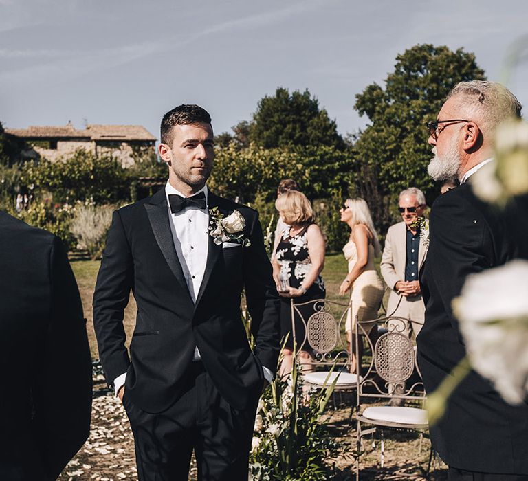 Groom in black-tie and white floral buttonhole during outdoor wedding ceremony