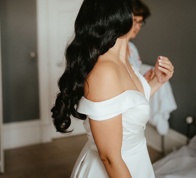 Bride wears off-the-shoulder wedding dress and her dark hair in curls 