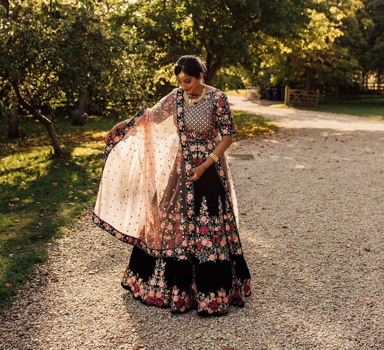 Bride wears red, pink and black floral embellished lehenga during golden hour 