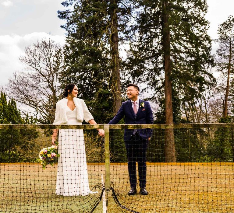 Bride wears faux fur coverup and stands beside her groom during outdoors couples portraits 