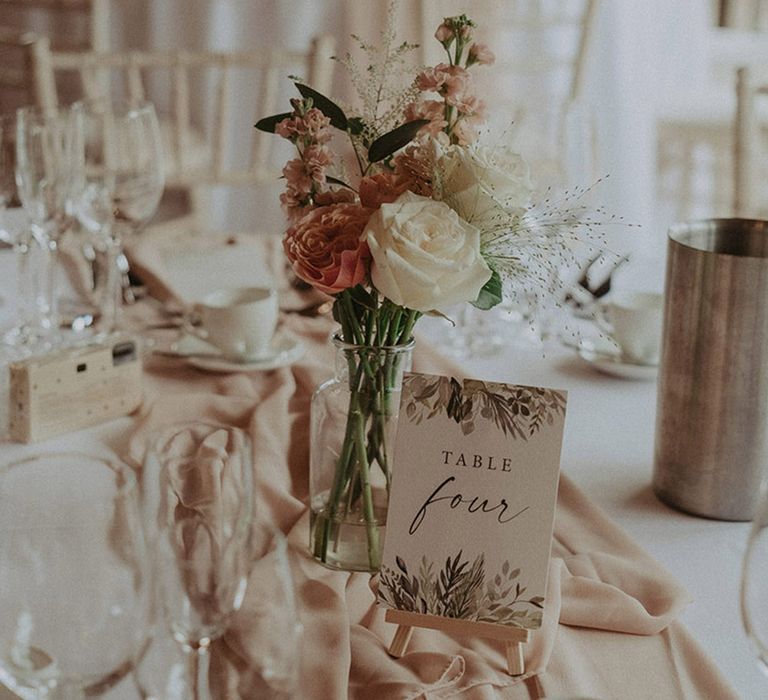 Pale pink table runner with pink and white wedding flower arrangement centrepieces including roses in small glass vases for the rustic luxe wedding