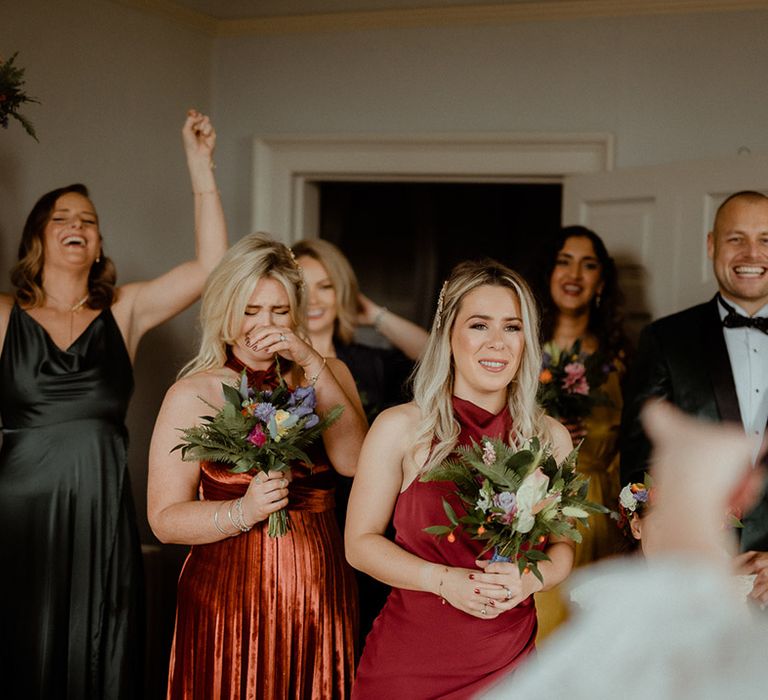 Groomsmen in black tie and bridesmaids in mismatched bridesmaid dresses celebrate as they get their first look at the bride on her wedding day