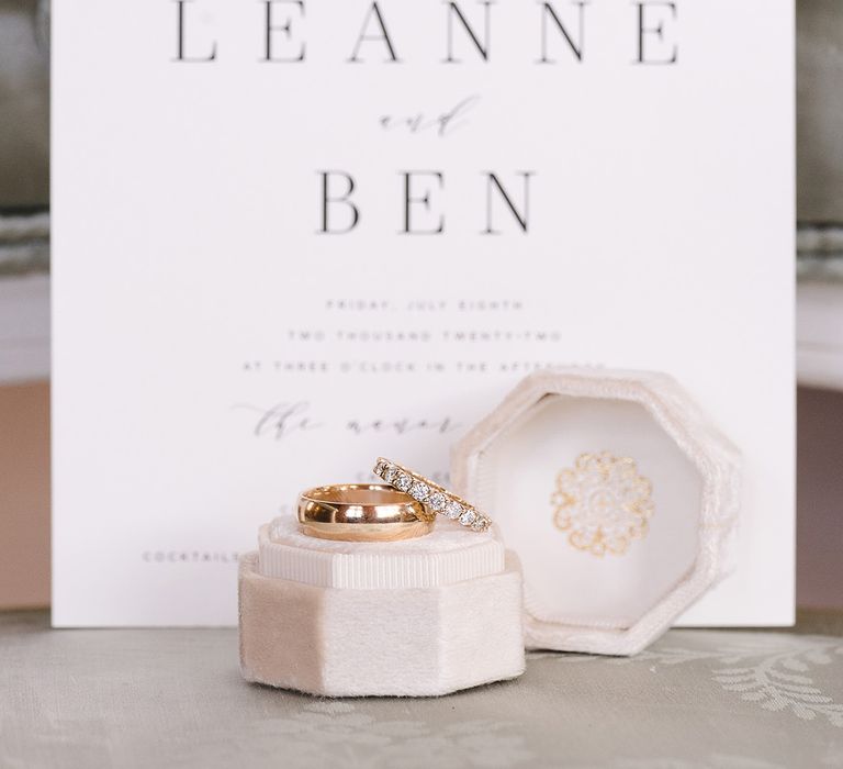 The groom's thick plain gold wedding band and the bride's diamond and gold wedding band in velvet ring box in front of the black and white wedding stationery