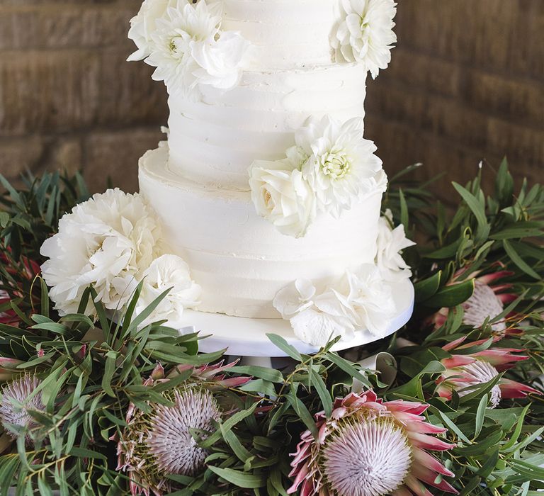 Three tier white iced wedding cake with white wedding flower decorations on white cake stand 