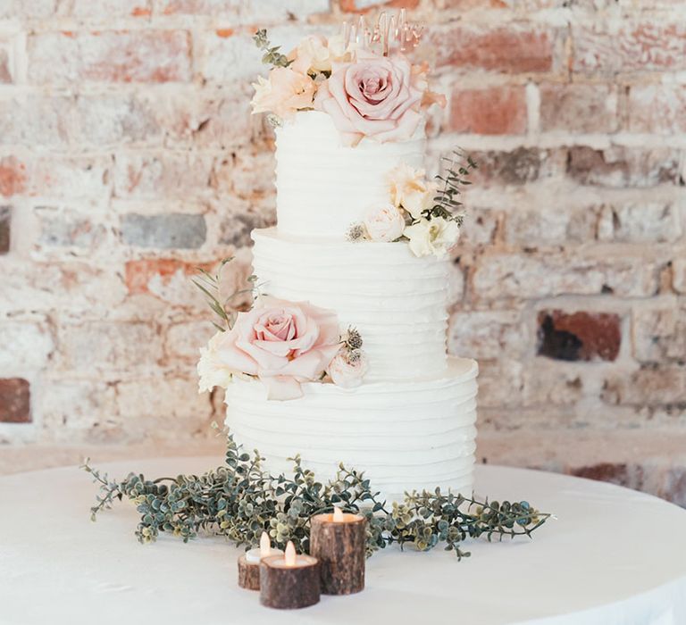 Three tier white wedding cake with pink rose wedding cake decoration with foliage details