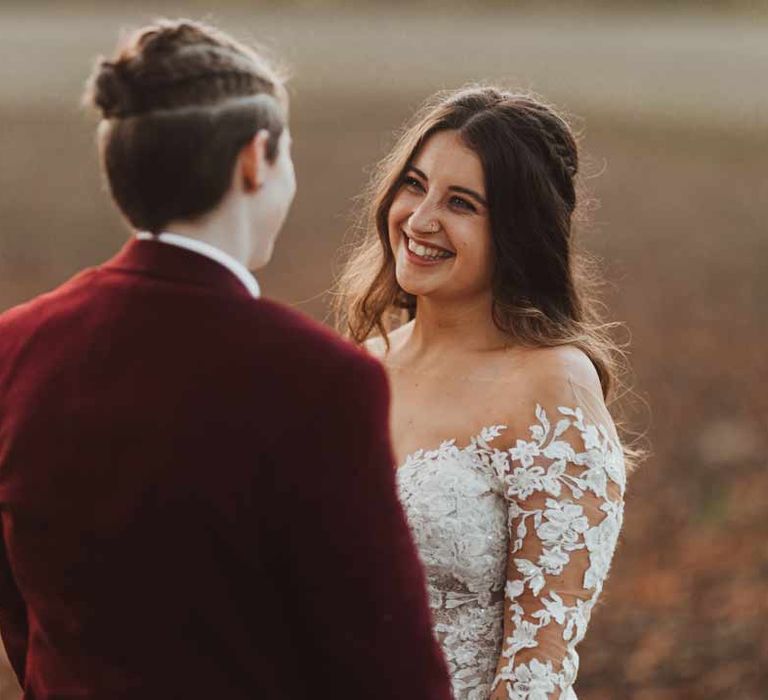 Bride in maroon bridal suit with bride in long sleeve lace illusion sleeve wedding dress with overlay 