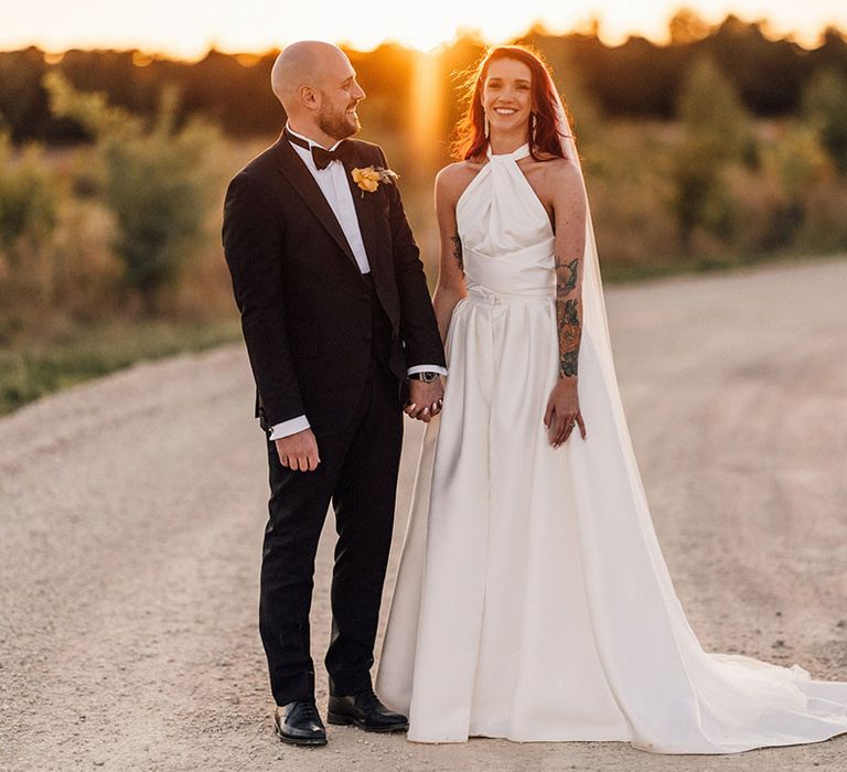 Groom in black tuxedo standing with the bride in a Halfpenny London wedding dress and black wedding shoes by Manolo Blahnik during golden hour 