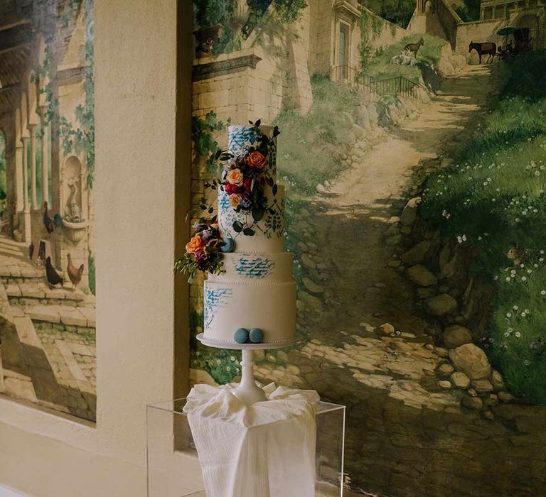 Four tiered toile wedding cake with white and blue icing and spring floral wedding cake toppers with blue macaroons 