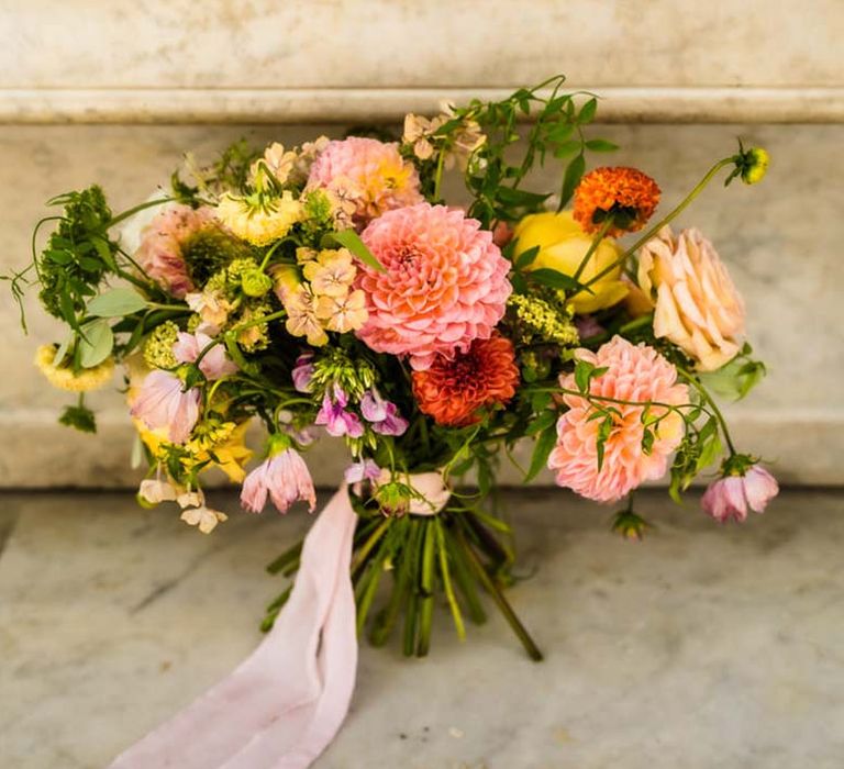 Vibrant pink, yellow, and orange bridal bouquet tied with pink ribbon including dahlias and roses 