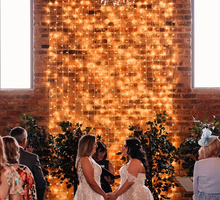 Same sex wedding with the two brides wearing gorgeous lace wedding dresses in front of fairy light altar decor 