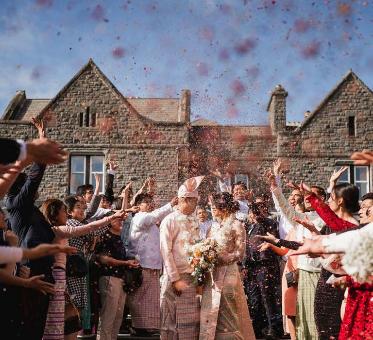 Bride in floral 3D applique pink and rose gold htamane standing with groom in baby pink htaingmathein doing colourful wedding confetti exit 