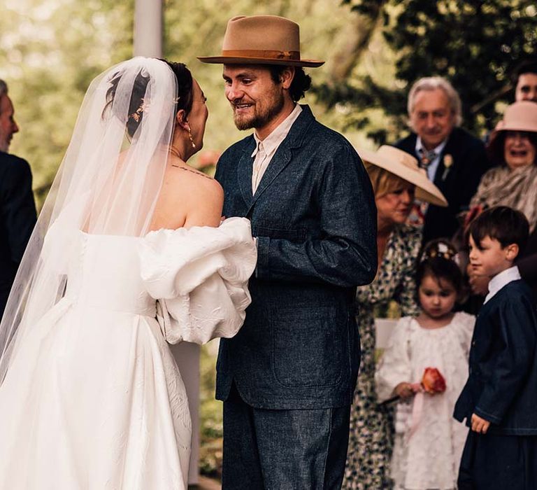 Bride in statement wedding dress leaning in for a kiss with the groom wearing stylish hat