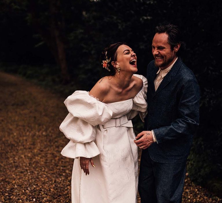 Bride in Jesus Peiro wedding dress smiling for couple photos with the groom in a denim suit and hat 