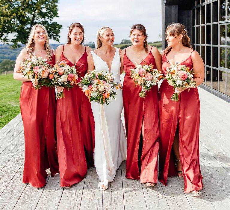 Bridal party wearing thigh split satin autumnal red dresses with bride at Botley Hill Barn wedding