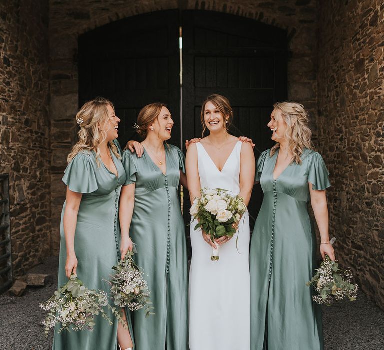 Bridal party wedding photo of the bridesmaids in short sleeve green satin dresses with the bride in a minimalist dress