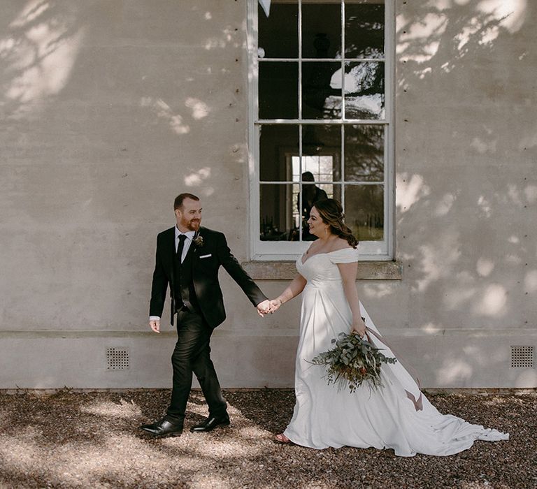 Madi Lane off the shoulder wedding dress walking with the groom after their special first look moment 