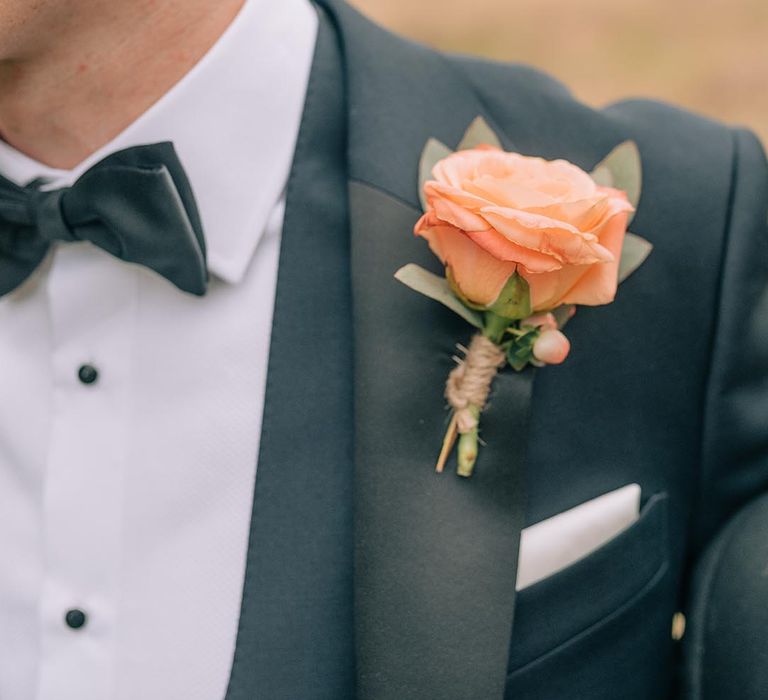 Groom in black tuxedo with coral rose buttonhole accessory 