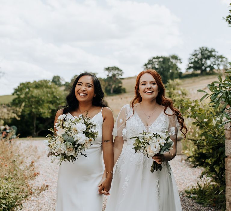 Bride in satin slip wedding dress with the bride in a floral lace princess gown for same sex wedding 