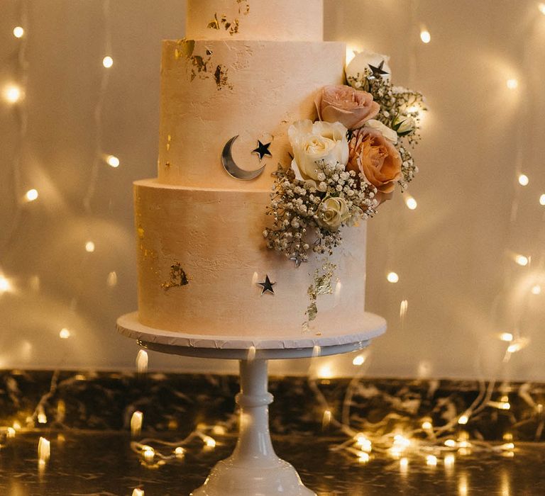 Three tier frosted wedding cake with gold moon and stars decorations with white gypsophila and small roses 