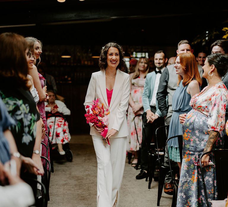 Bride in white suit and pink heart shaped top walks herself down the aisle 