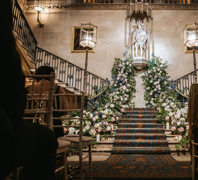 Pastel pink, purple and blue wedding flowers line the aisle at historic wedding venue 