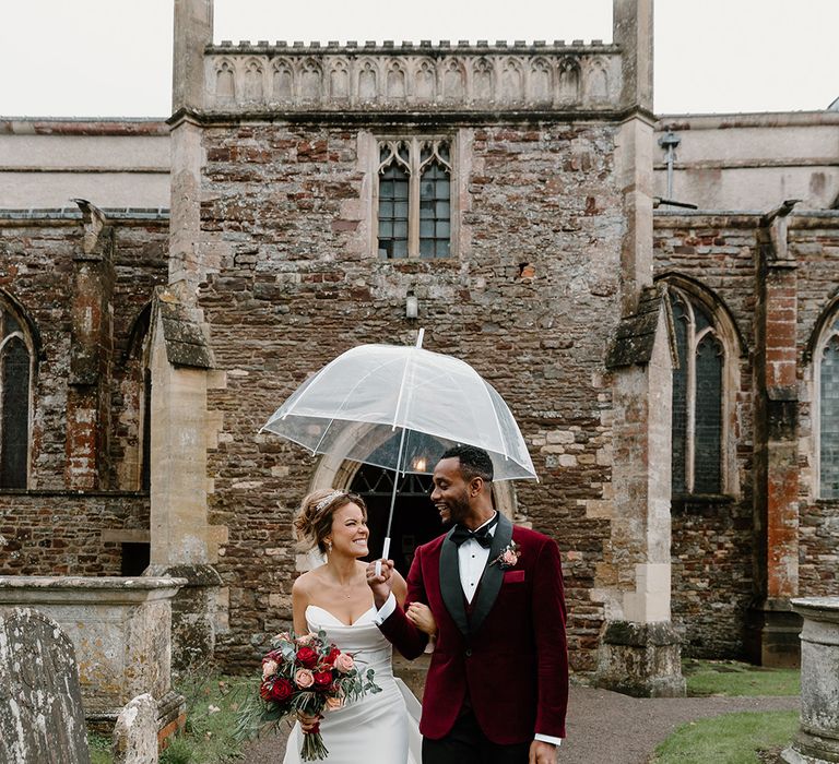 The bride and groom walking underneath a clear umbrella on their wedding day 