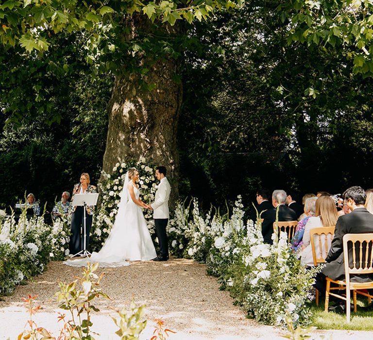 Beautiful outdoor wedding ceremony decorated with all white wedding flowers lining the aisle and as an arch for the altar space 