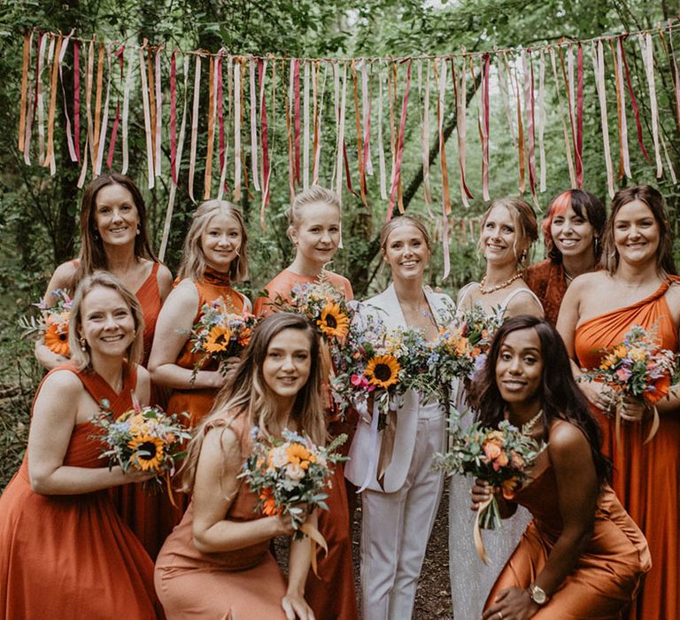 Bridal party wearing burnt orange bridesmaid dresses holding sunflower bouquets 