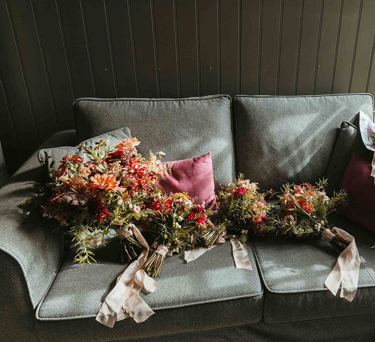 Bridal party bouquets resting on blue sofa made form natural autumnal flowers 