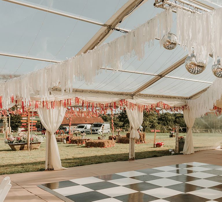 Marquee wedding with checkered black and white dance floor decorated with disco balls and DIY bunting for at home wedding 