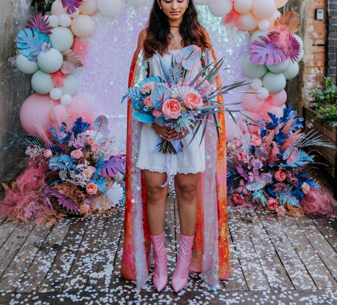 Stylish bride in short dress, cape, boots and crown at festival wedding 