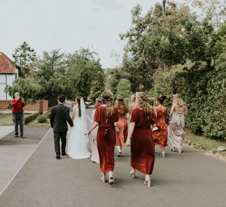 Bridesmaids in different coloured oranges dresses walking through the village to the church