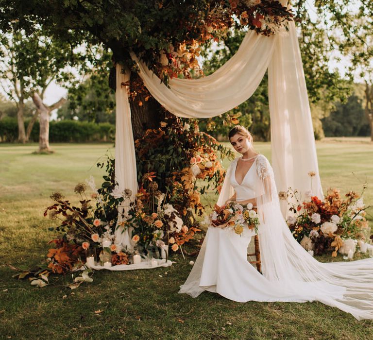 Bride sitting at a floral altar in the grounds of Reymerston Hall