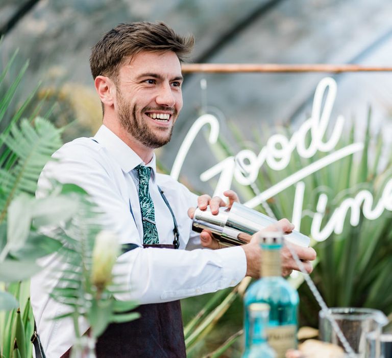 Smiling barman shakes cocktail in front of 'Good Times' neon sign at Urban Jungle Suffolk