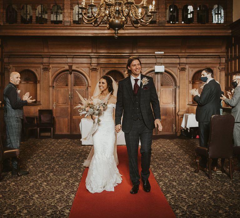 Bride and groom walking down the red carpet aisle at their Rhinefield House wedding 