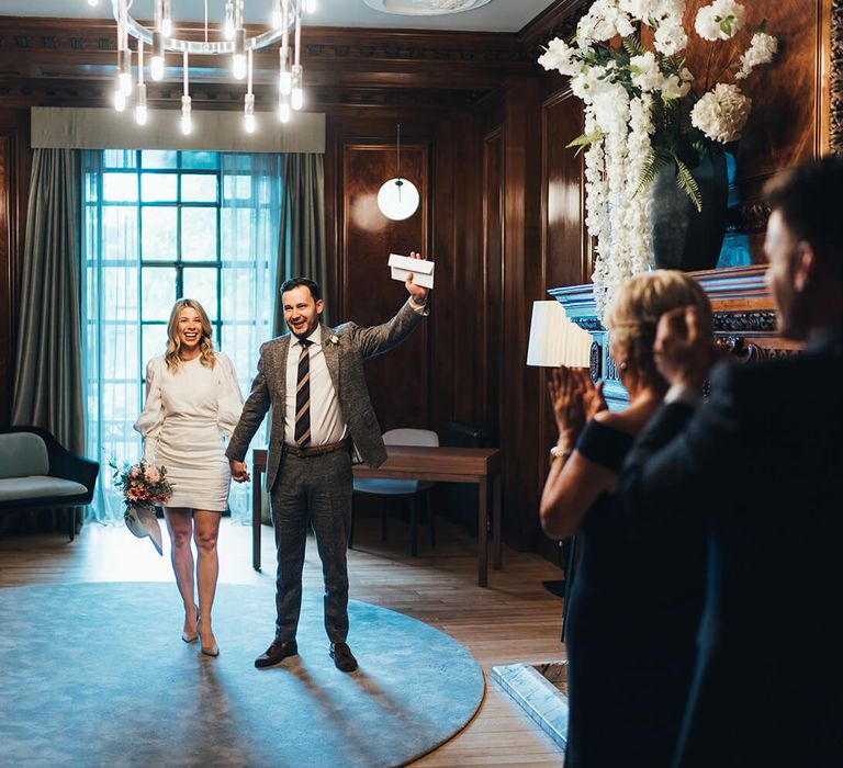 Newly wed couple at townhall wedding with groom raising his arm in celebration and short bridal wedding dress 