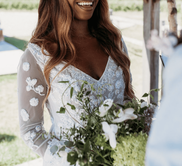 A Black bride with long loose wavy hair wears a white flower crown and smiles to the groom.