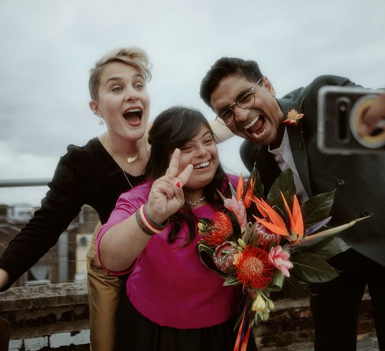 Selfie with bridesmaid in pink and green lenghas holding a tropical flower bouquet and groomsman in a teal suit 