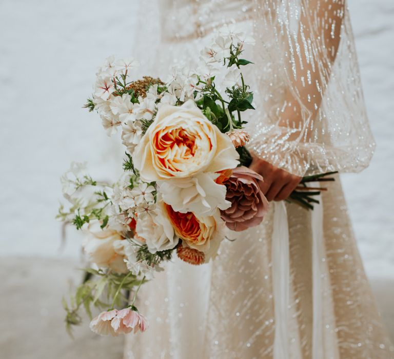 The bride holding orange and blush wedding flowers against her sparkly wedding dress